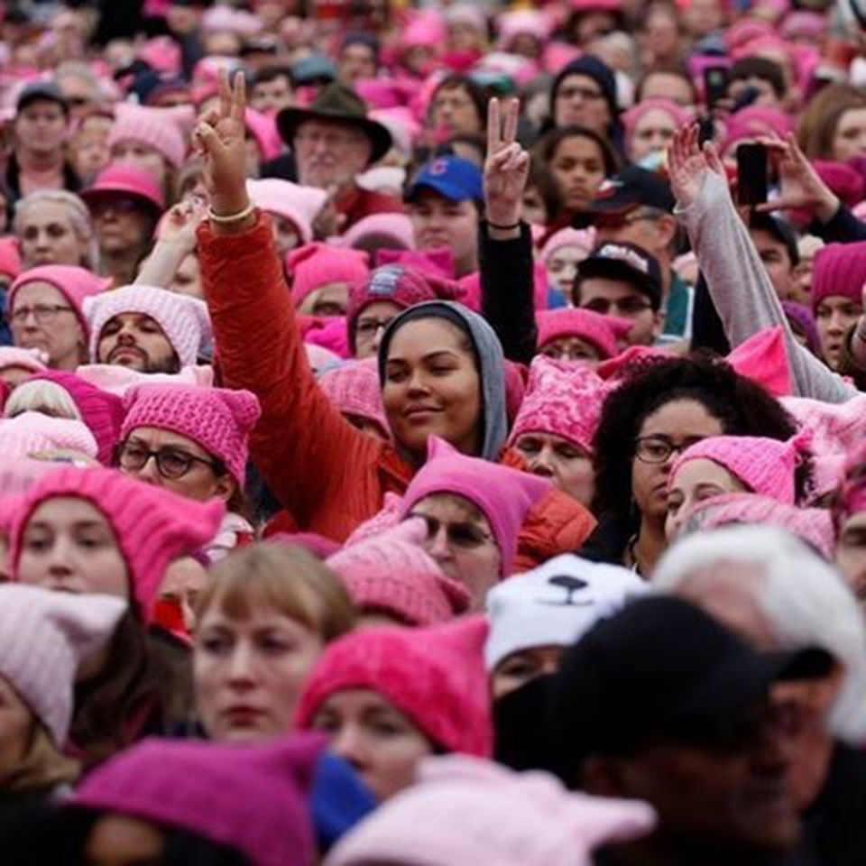 ピンク色のネコの耳の形をした毛糸で編まれた帽子をかぶったたくさんのデモ参加者